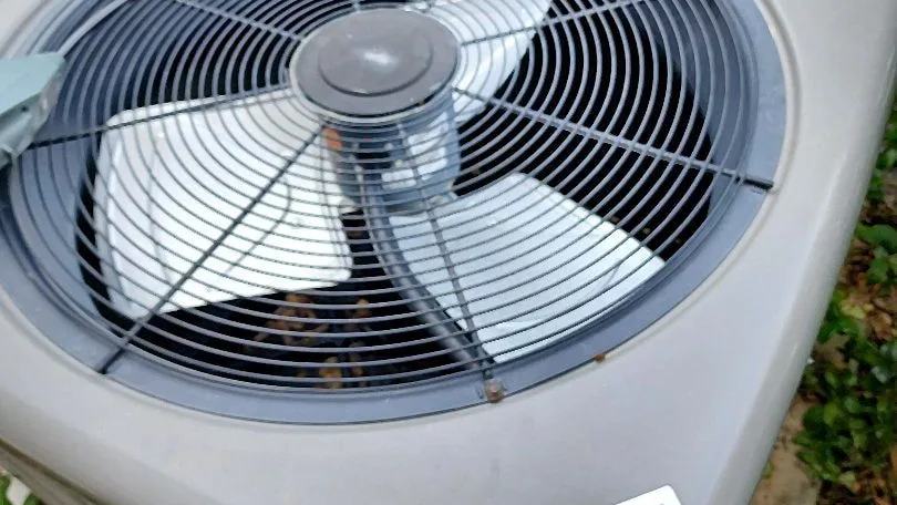 Close-up of a condenser fan grille with a 24/7 emergency service sticker