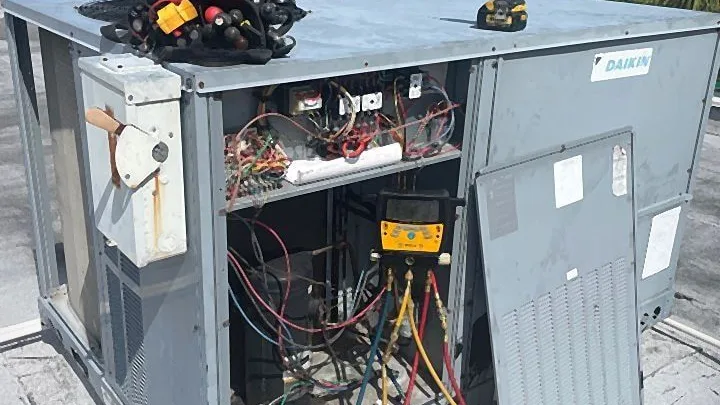 Technician tools and digital manifold gauges on an open rooftop packaged unit during repair