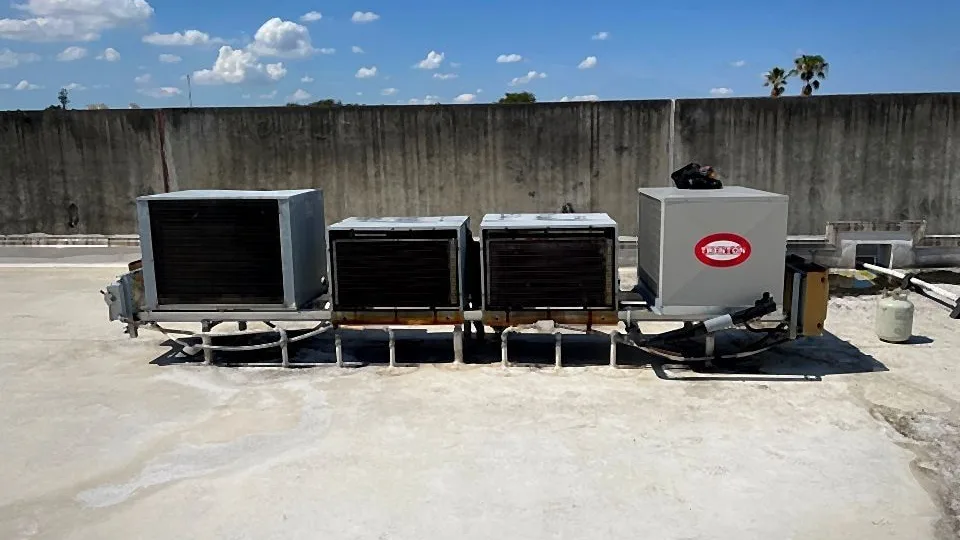Row of commercial refrigeration condensing units on a rooftop rack with interconnecting piping