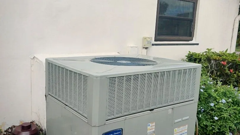 Packaged air conditioning unit on a concrete pad beside a stucco home