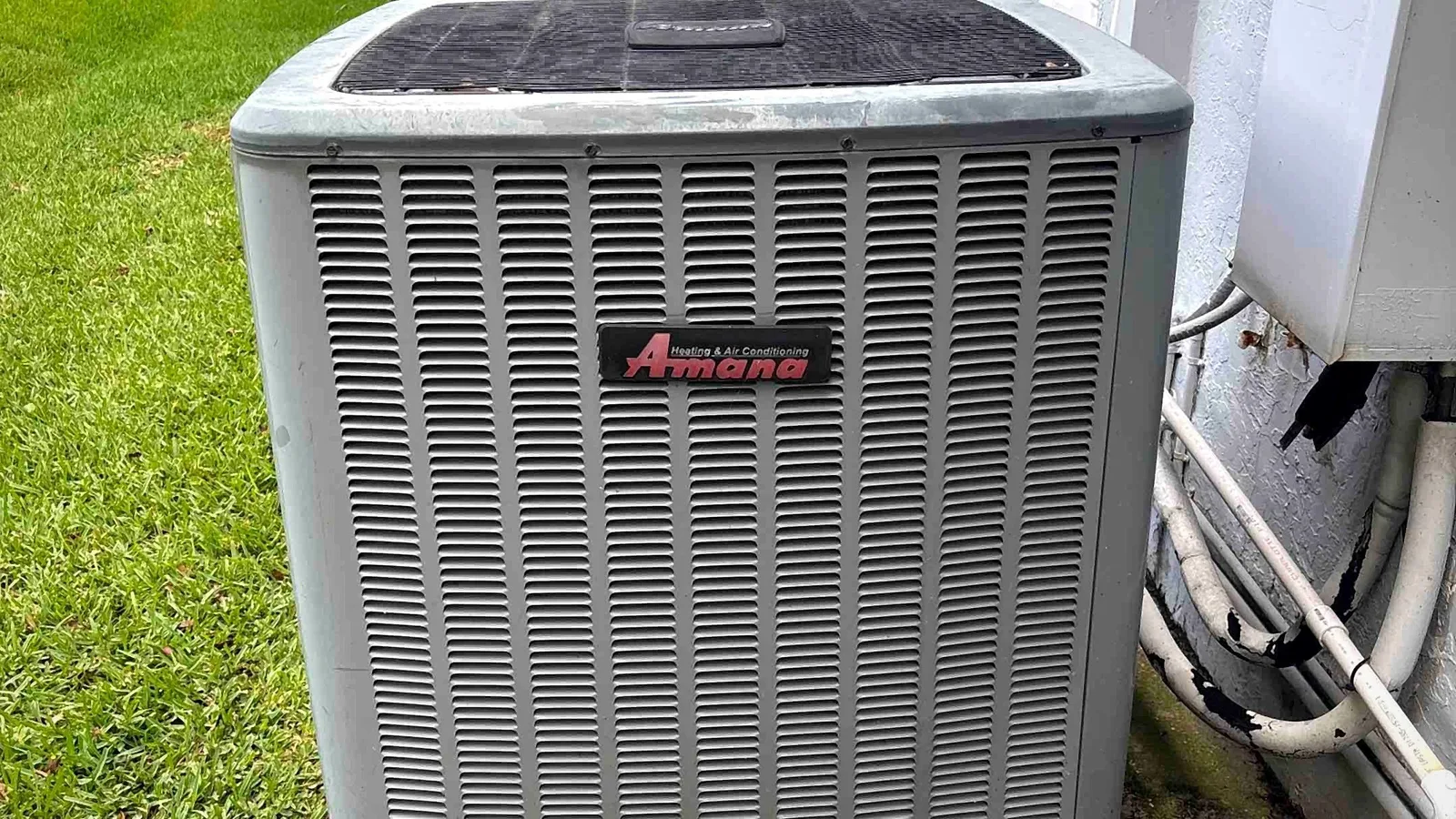 Amana condenser with hurricane tie-down straps installed on a slab beside a landscaped lawn