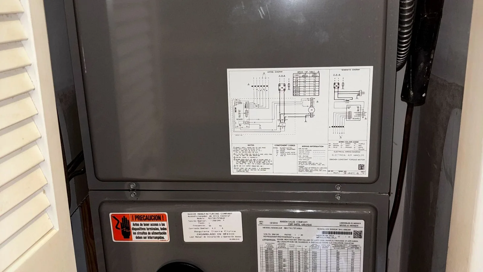 Air handler installed in a louvered utility closet with labeled data plate and refrigerant lines
