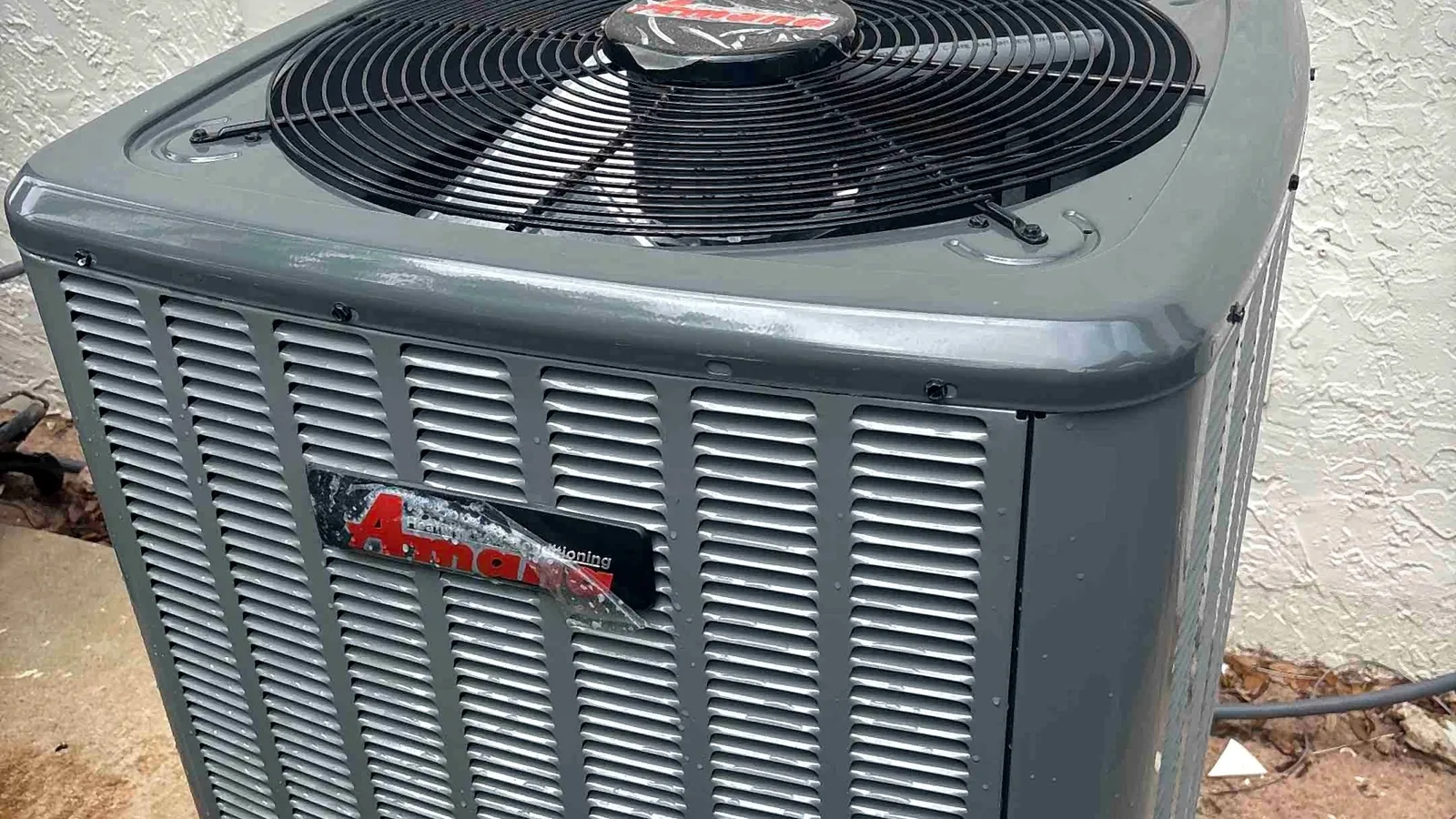 New Amana outdoor condenser installed on a concrete slab beside a stucco home