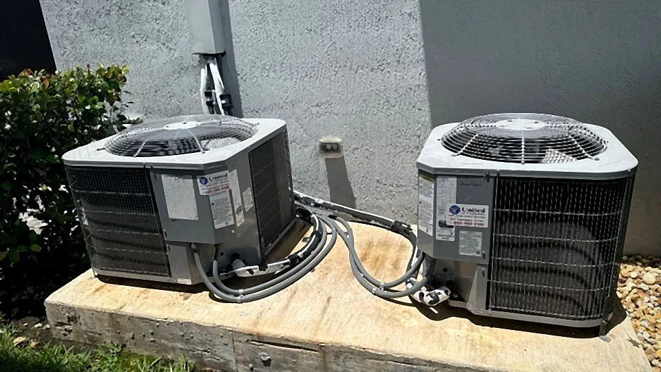 Two residential condensers side by side on a shared concrete pad with tidy refrigerant linesets