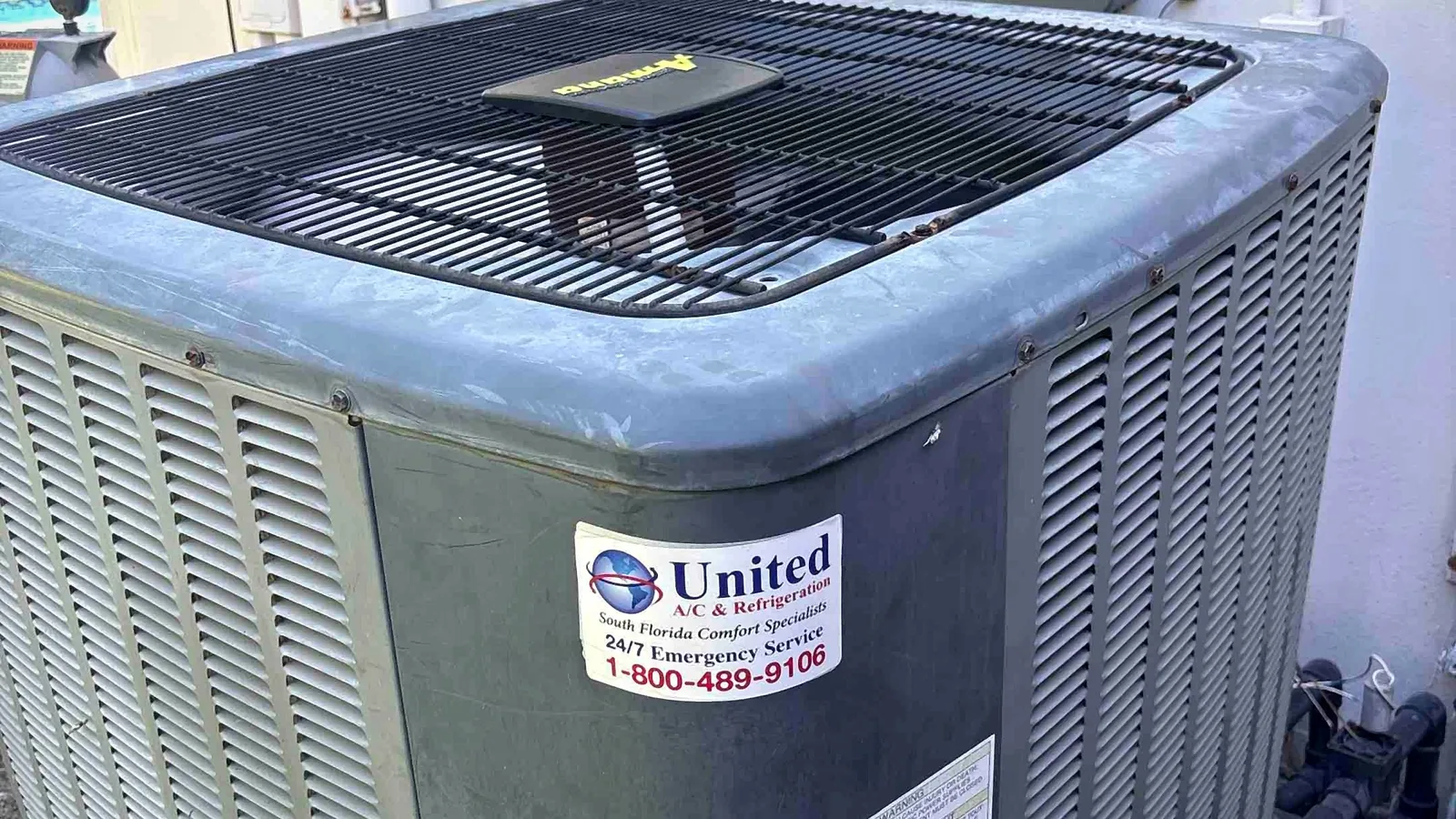 Amana condenser installed beside a home next to electrical disconnects and pool equipment