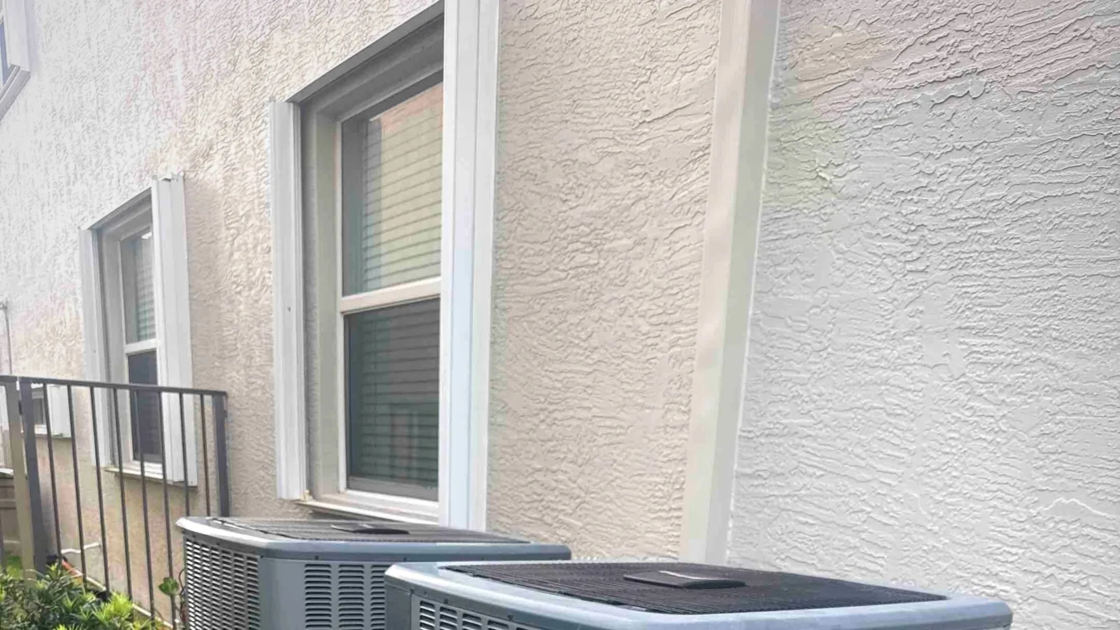 Two residential condensers sharing a concrete pad in a townhome side yard