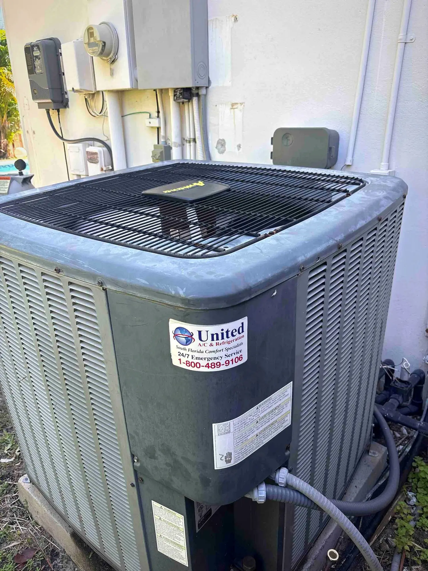 Amana condenser installed beside a home next to electrical disconnects and pool equipment