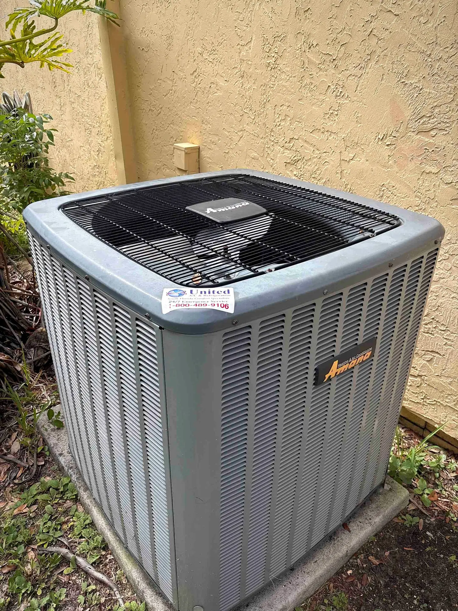 Amana outdoor condensing unit installed on a concrete pad beside a stucco home