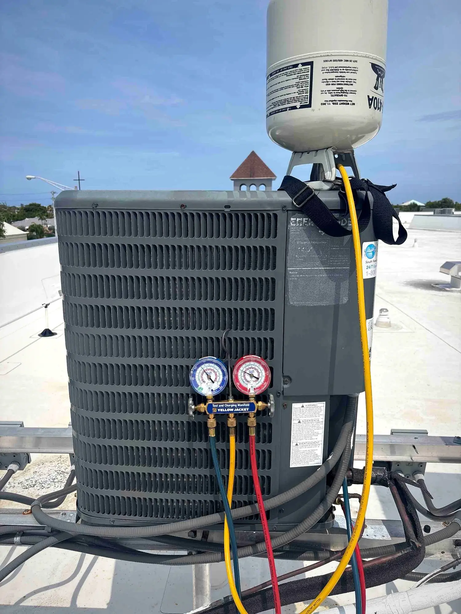 Technician charging a rooftop condenser with R-410A refrigerant using manifold gauges
