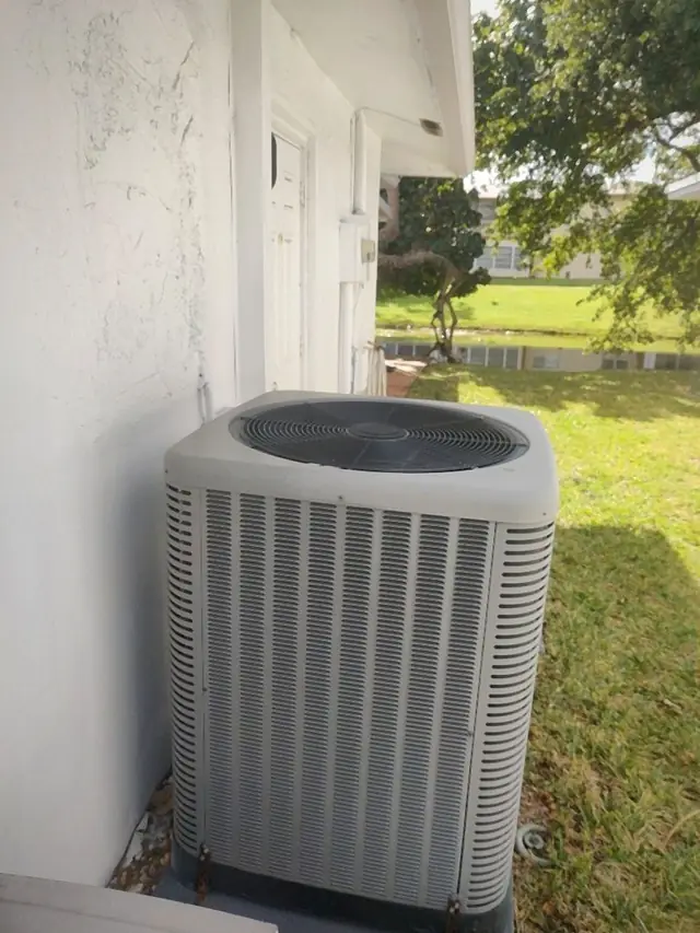 Residential air conditioning condenser installed on a pad beside a home exterior wall