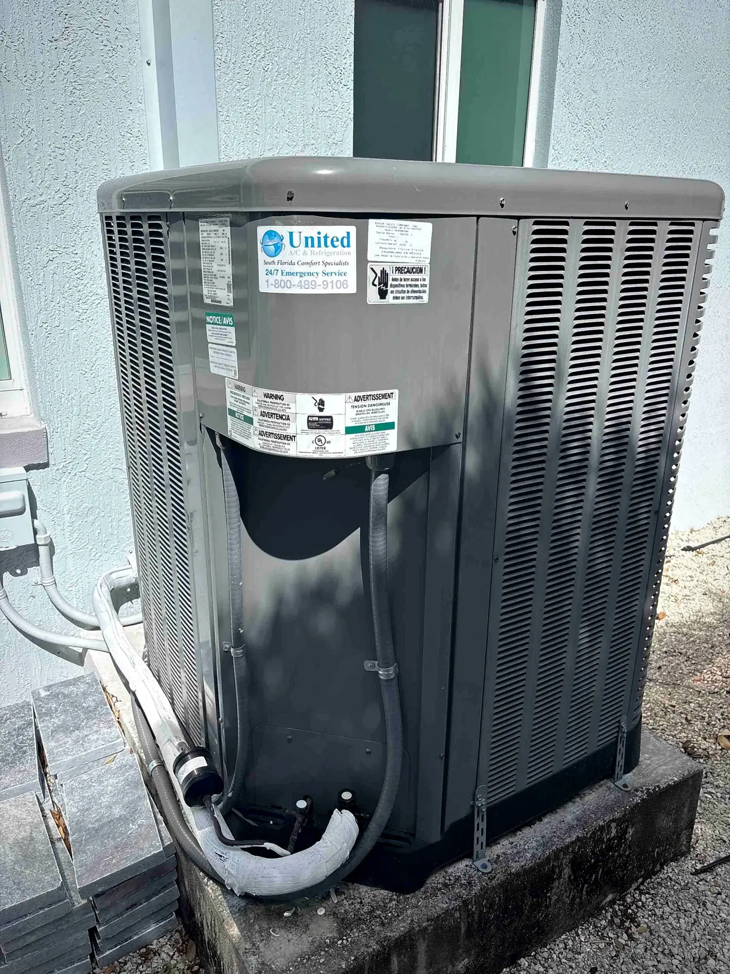 Outdoor HVAC unit on a raised concrete curb with flexible whips and insulated refrigerant lines