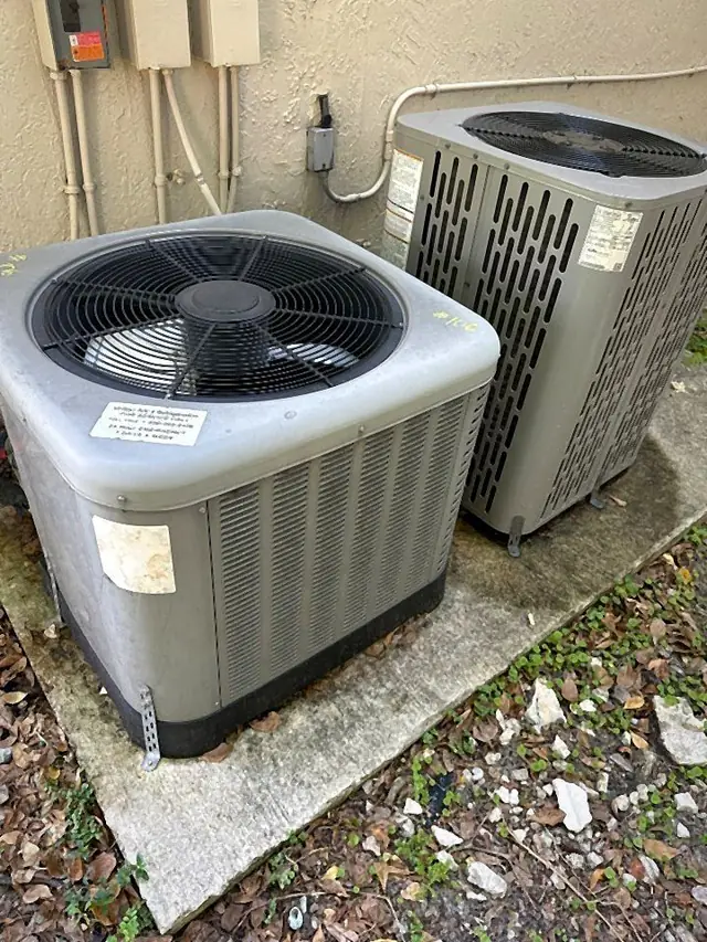 Two residential condensers on side-yard pads with refrigerant lines and electrical disconnects