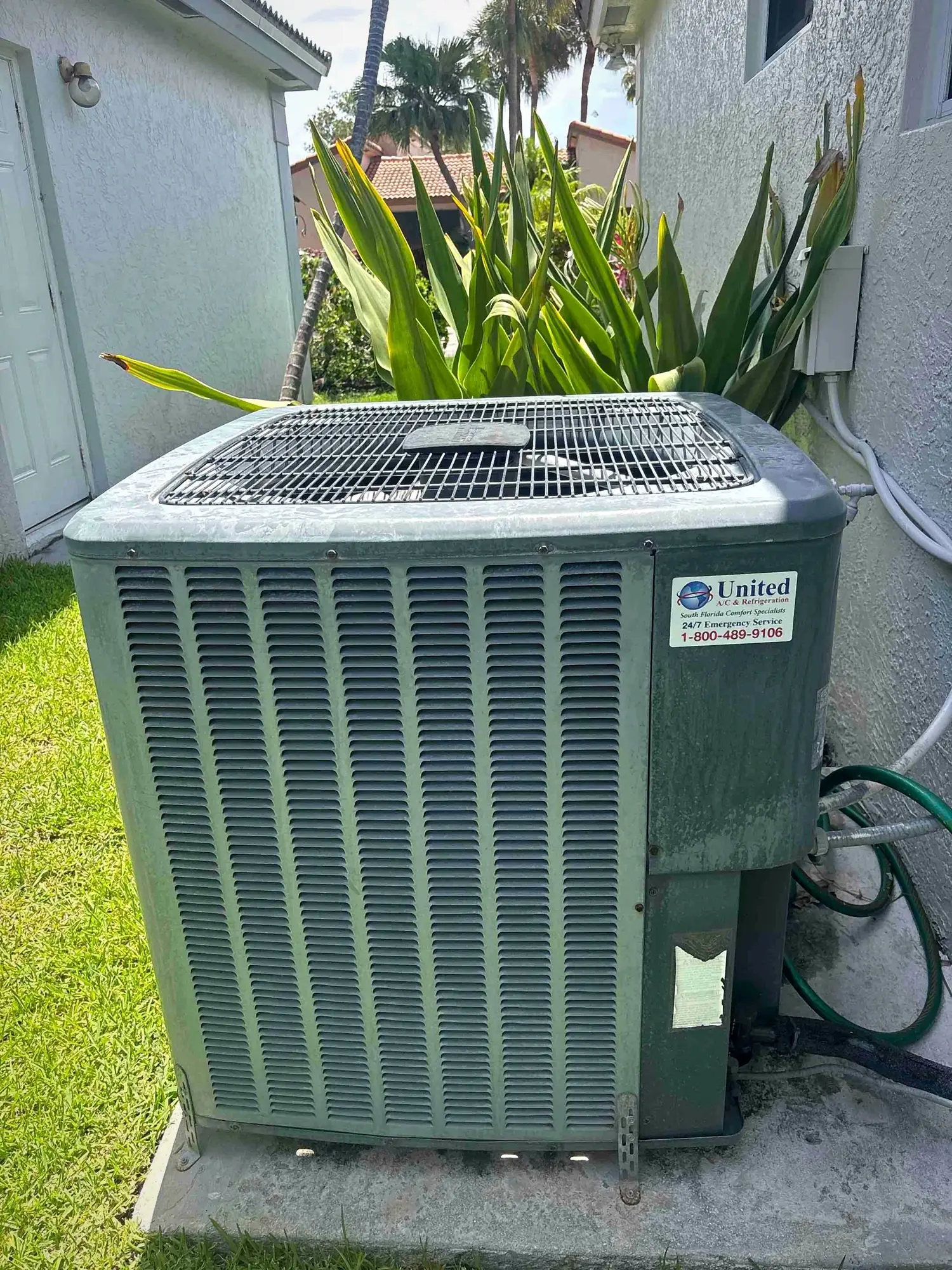 Residential condensing unit on a slab beside a home with tropical landscaping