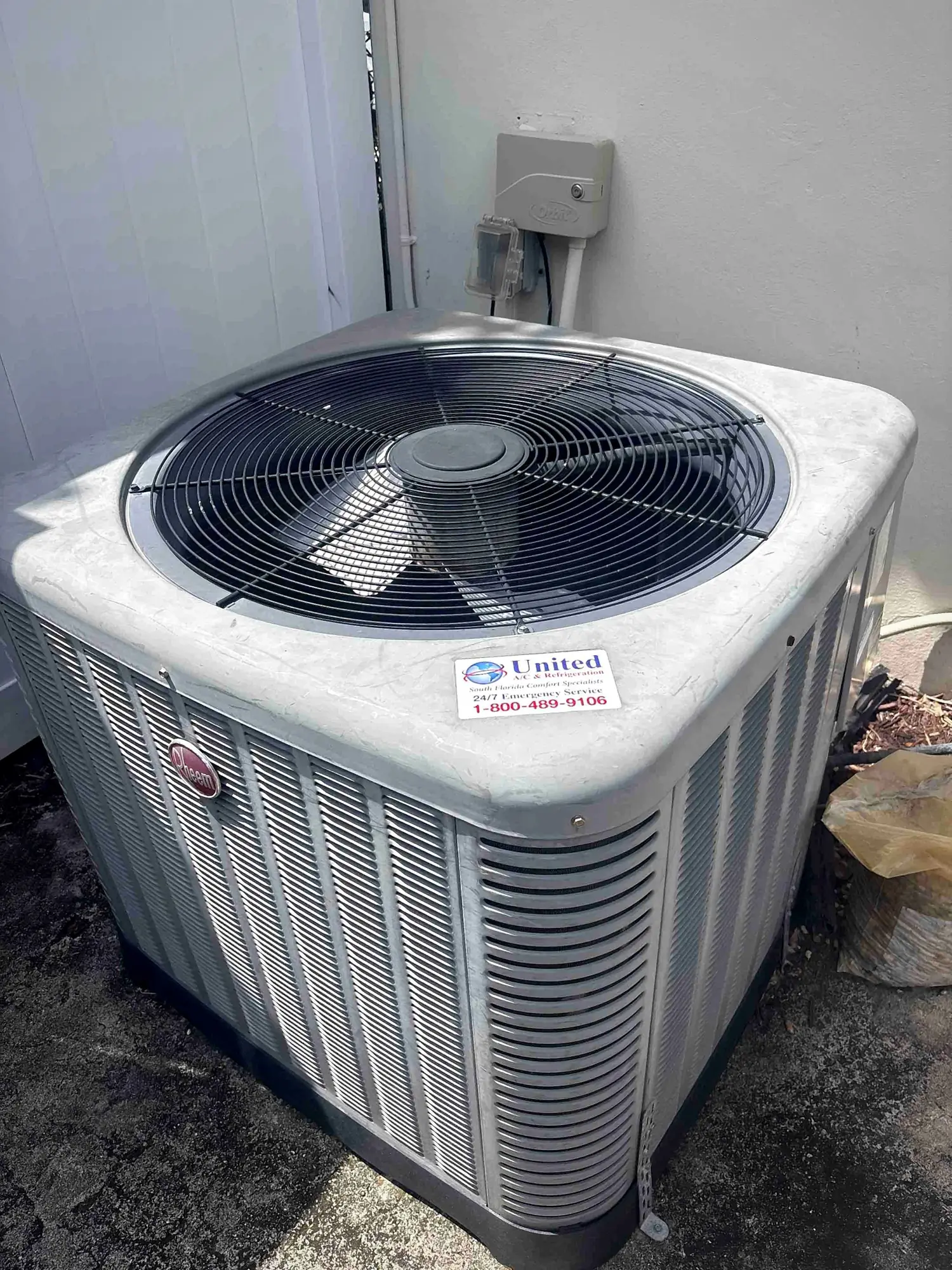 Clean condenser unit beside a home with wall-mounted electrical disconnect above