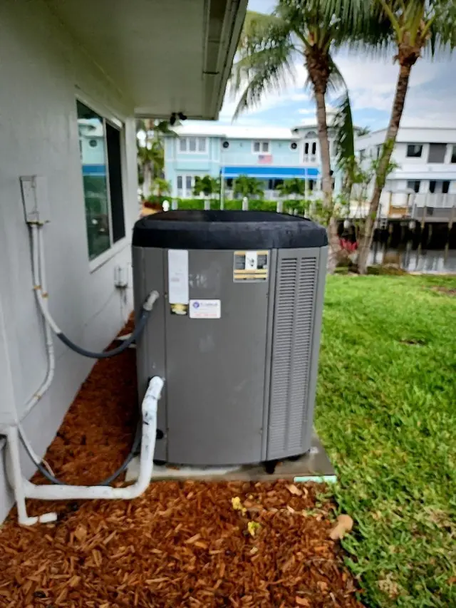 Residential condenser beside a waterfront home with neatly routed refrigerant and drain lines