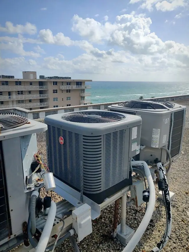 Condensers on an oceanfront rooftop with refrigerant linesets and one unit opened for service