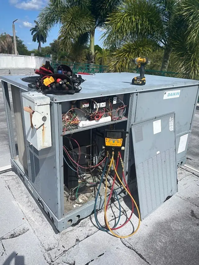 Technician tools and digital manifold gauges on an open rooftop packaged unit during repair