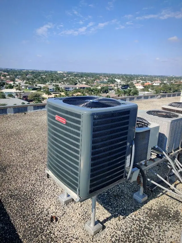 Condenser elevated on stands atop a high-rise roof overlooking a palm-lined neighborhood
