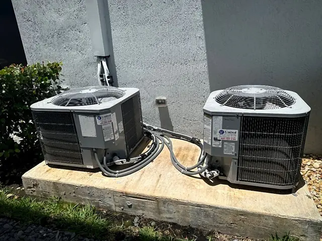 Two residential condensers side by side on a shared concrete pad with tidy refrigerant linesets